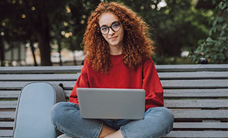 Junge Frau sitzt auf einem Bank und arbeitet an einem Laptop