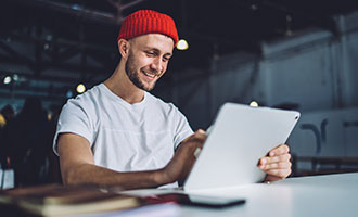 Junger Mann sitzt an einem Tisch und arbeitet mit einem Tablet